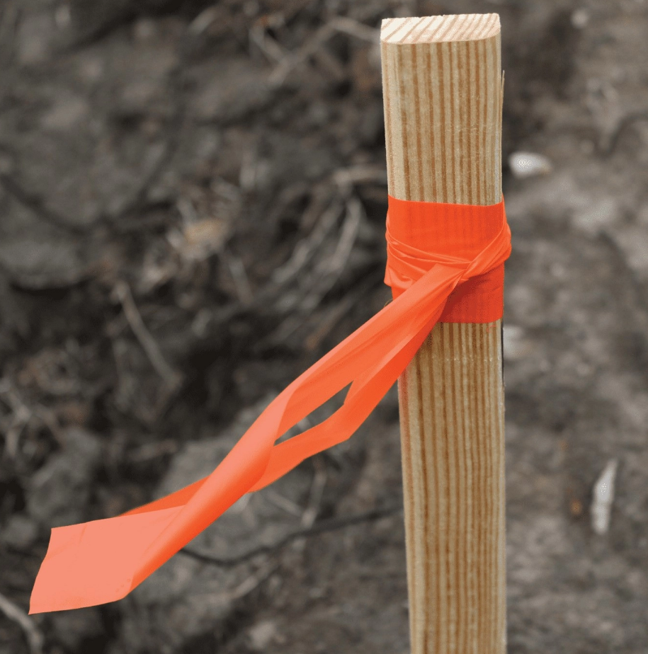 Orange flagging perfectly visible on a wooden stake for any engineers.